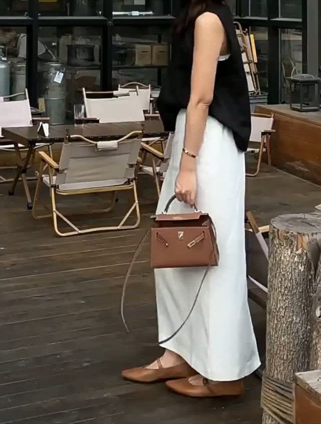 A person wearing a black top and a long white midi skirt standing on a wooden deck.