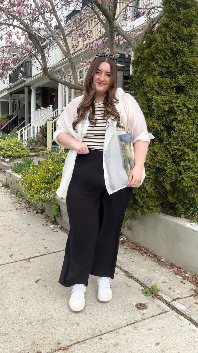 A woman wearing a striped top, white shirt, and black wide-leg trousers standing outdoors.