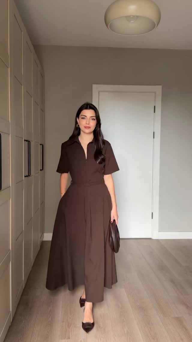 A woman wearing a brown midi dress and heels standing in a hallway.