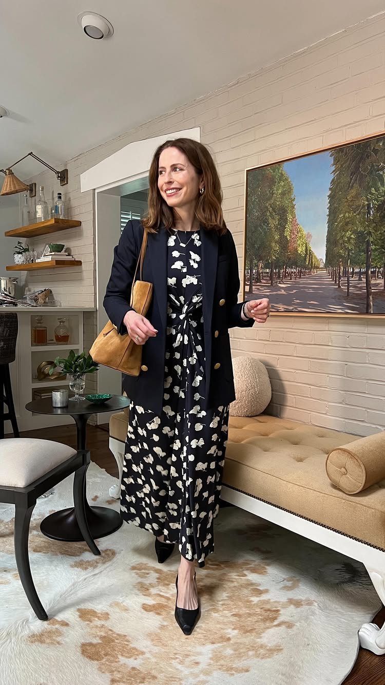 Woman wearing a navy patterned midi dress, navy blazer, and black heels in a living room.