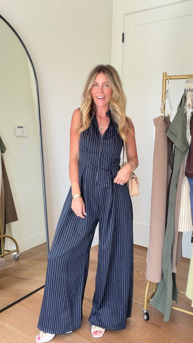 A woman wearing a navy blue pinstriped wide-leg jumpsuit and holding a small beige handbag.