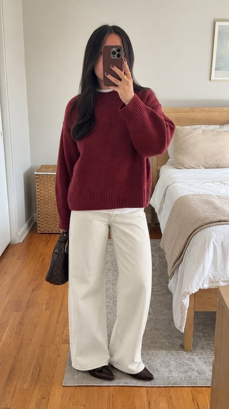Woman in a burgundy sweater and cream wide-leg trousers taking a mirror selfie.