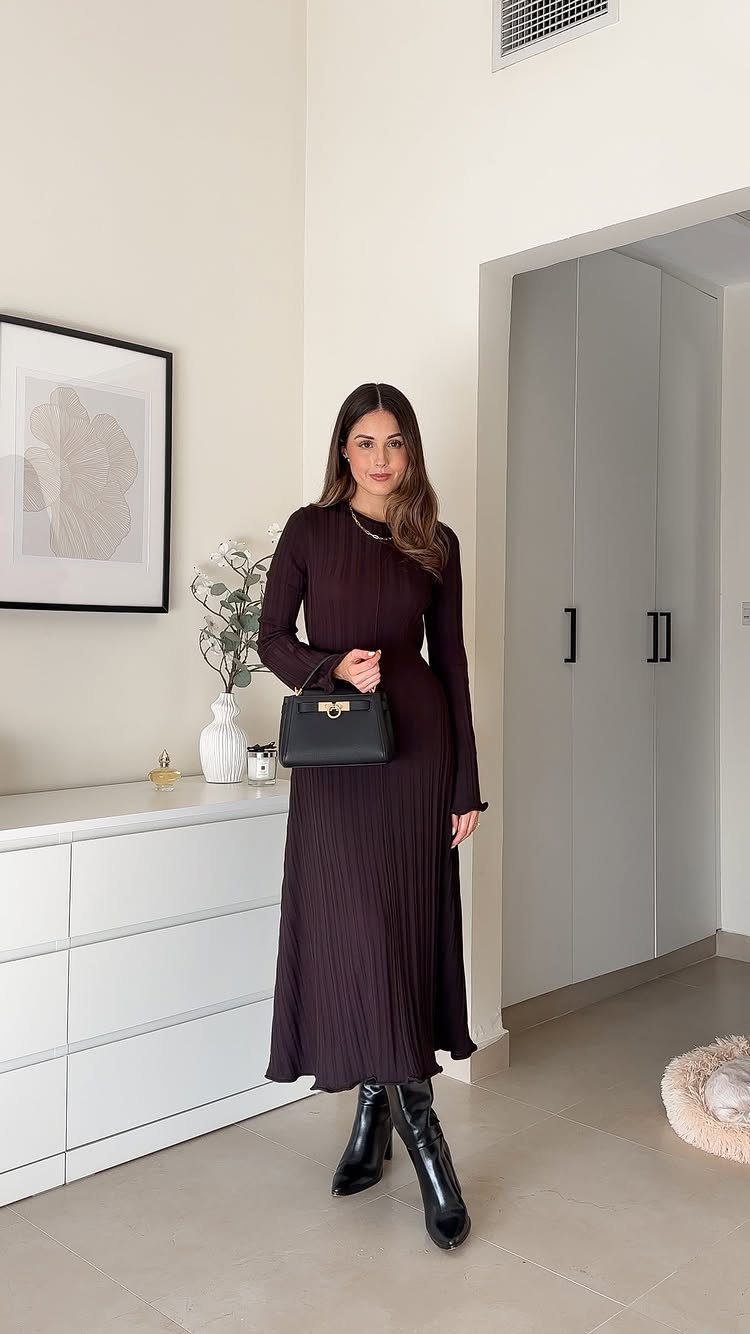 A woman wearing a long dark plum pleated maxi dress and black boots.