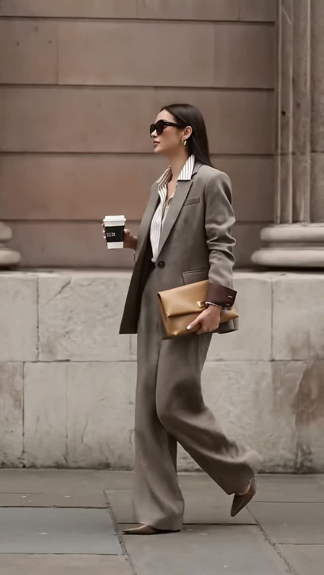 A woman in a taupe tailored blazer and matching wide-leg trousers walking through a city.