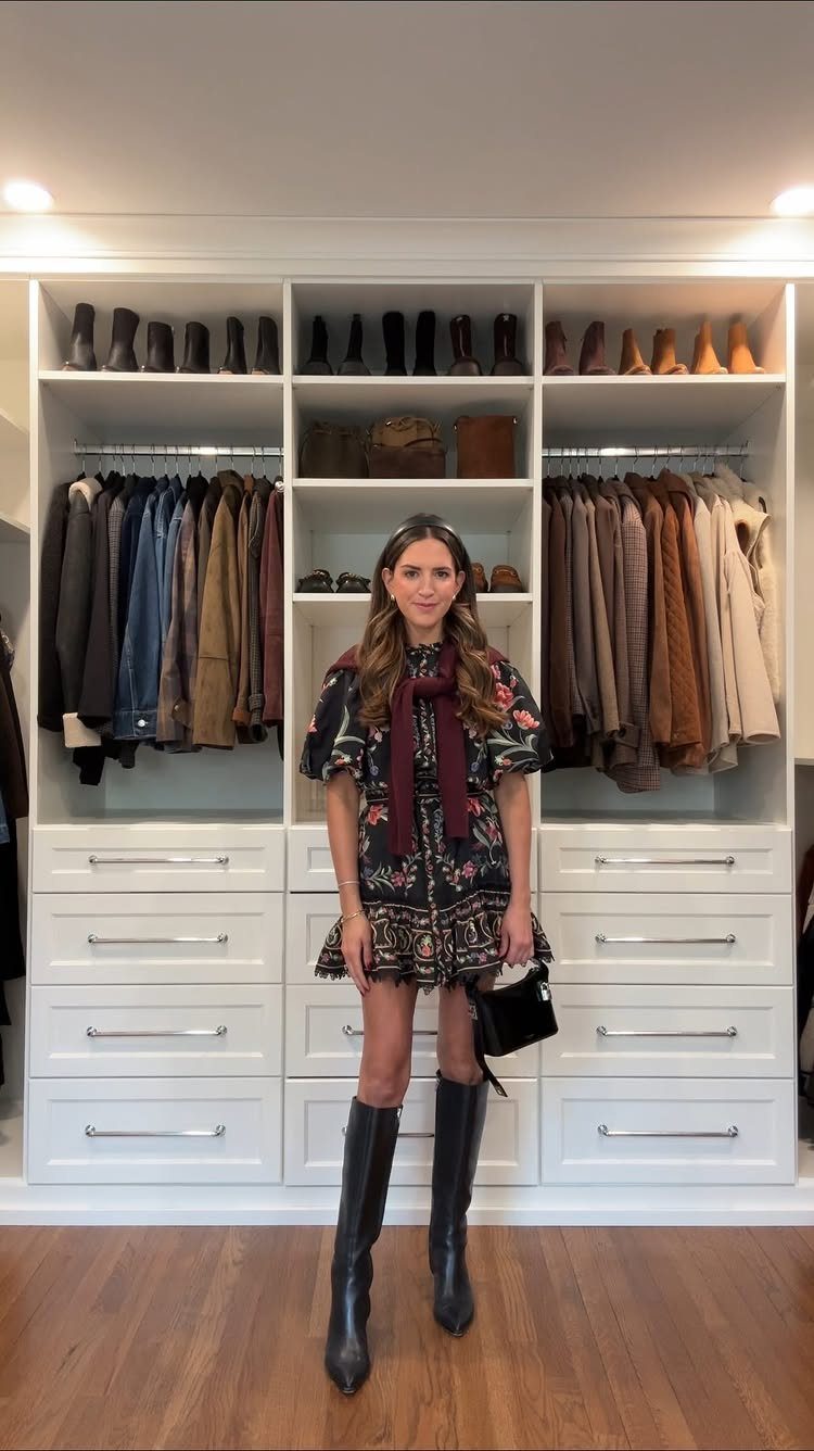Woman in a floral dress and tall black leather boots standing in a white closet.
