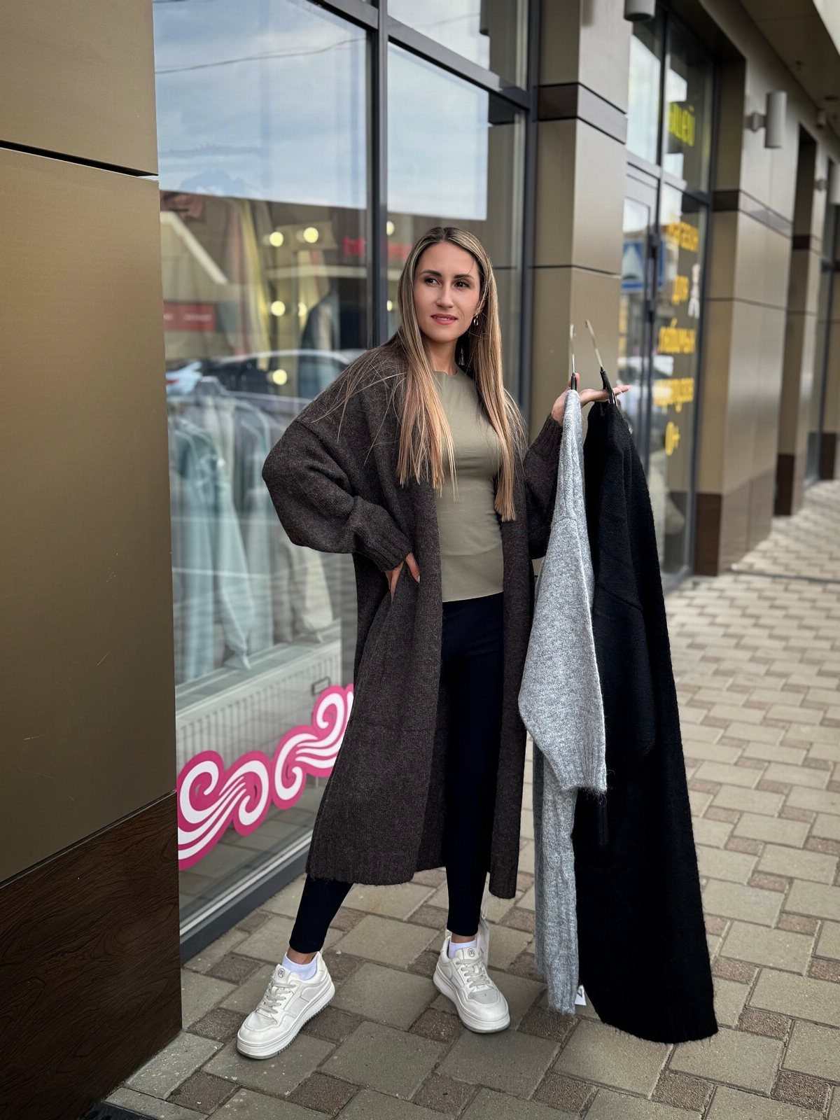 A woman wearing a long grey cardigan, green top, and black leggings standing outdoors.