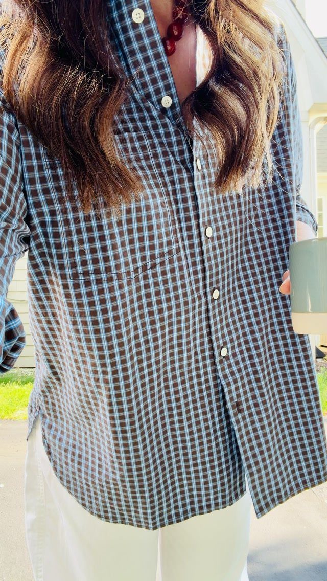 A person wearing a blue and brown checkered button-down shirt over white clothing.
