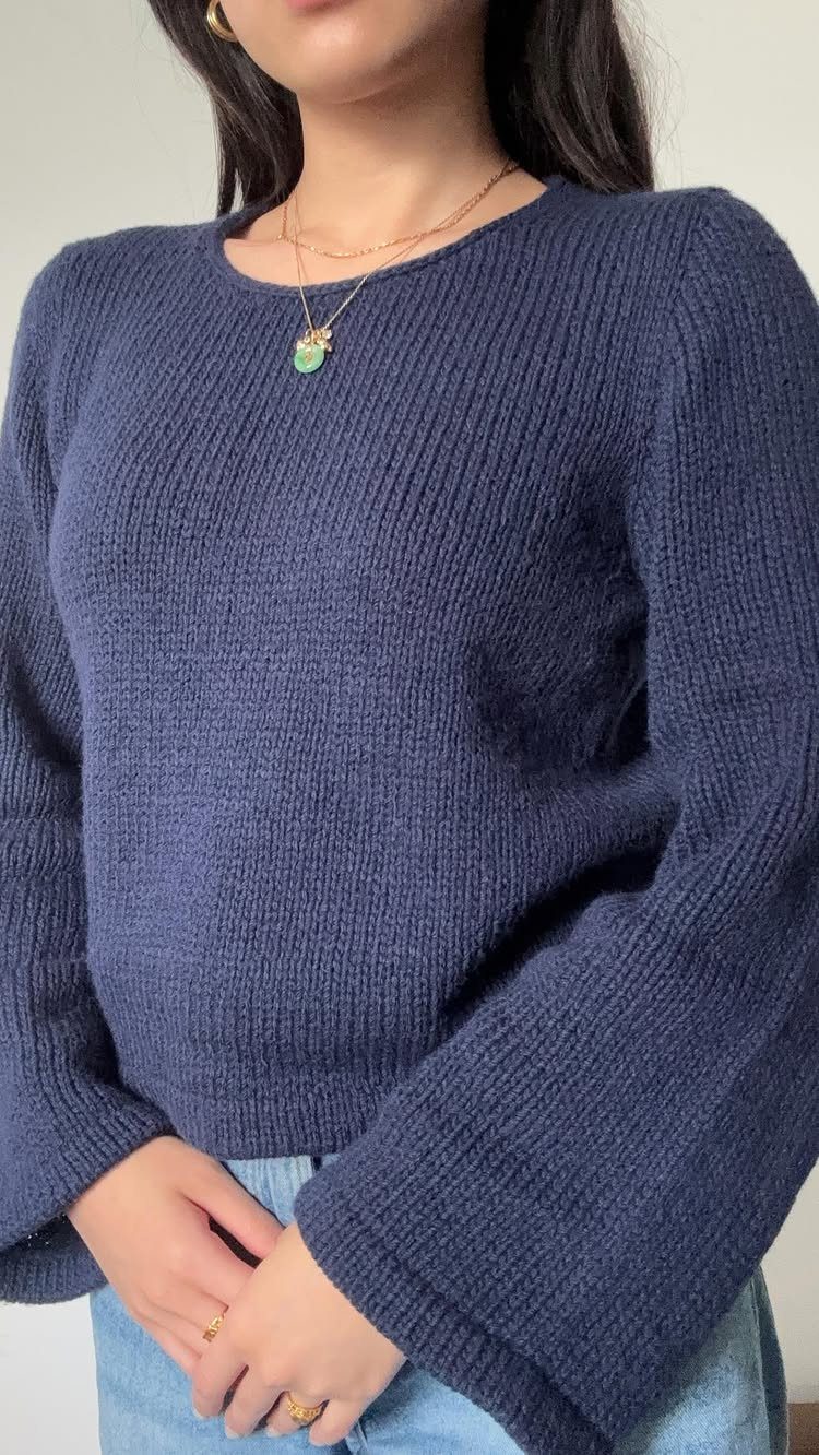 A person wearing a navy blue textured knit sweater and light blue denim jeans.
