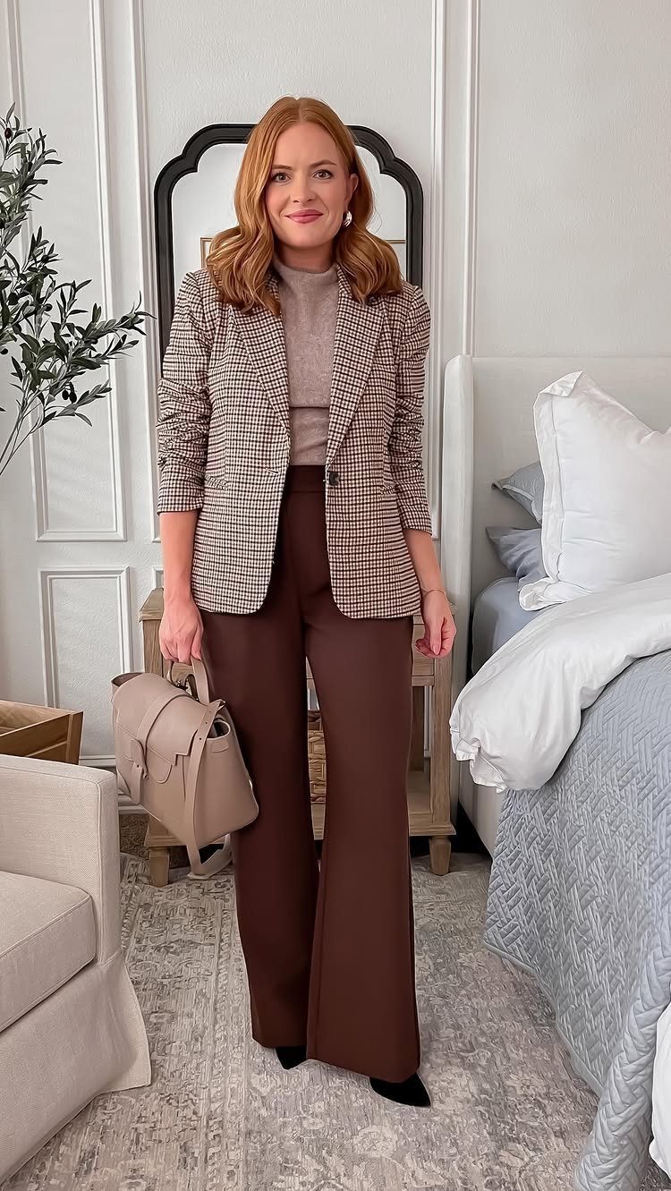 A woman wearing a plaid blazer, beige turtleneck, and brown wide-leg trousers standing in a room.