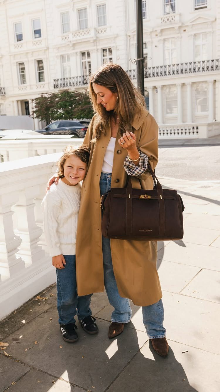 A woman in a tan trench coat holding a large dark brown structured leather tote bag.