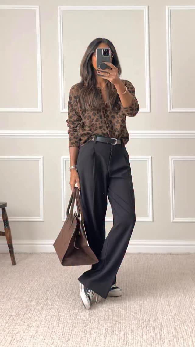 Woman in leopard print blouse and black wide-leg tailored trousers holding a brown tote bag.