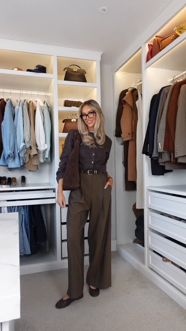 A woman posing in a white walk-in closet wearing olive wide-leg trousers and a dark top.
