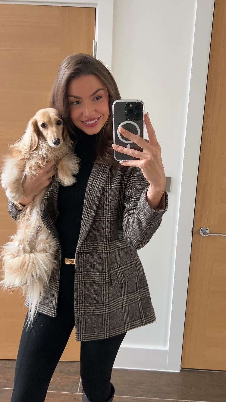 A smiling woman in a plaid blazer and black turtleneck holding a small dachshund.