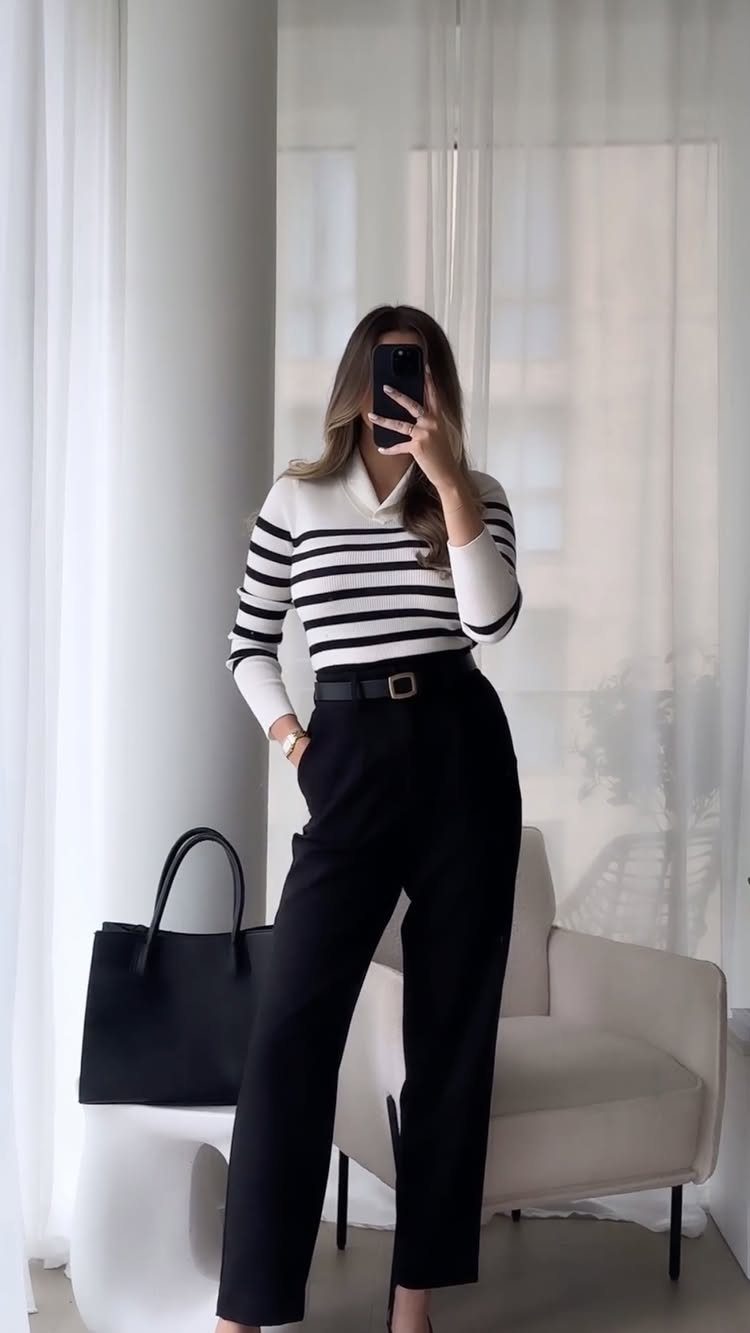 Woman in a striped long sleeve shirt and black high-waisted trousers posing for a selfie.