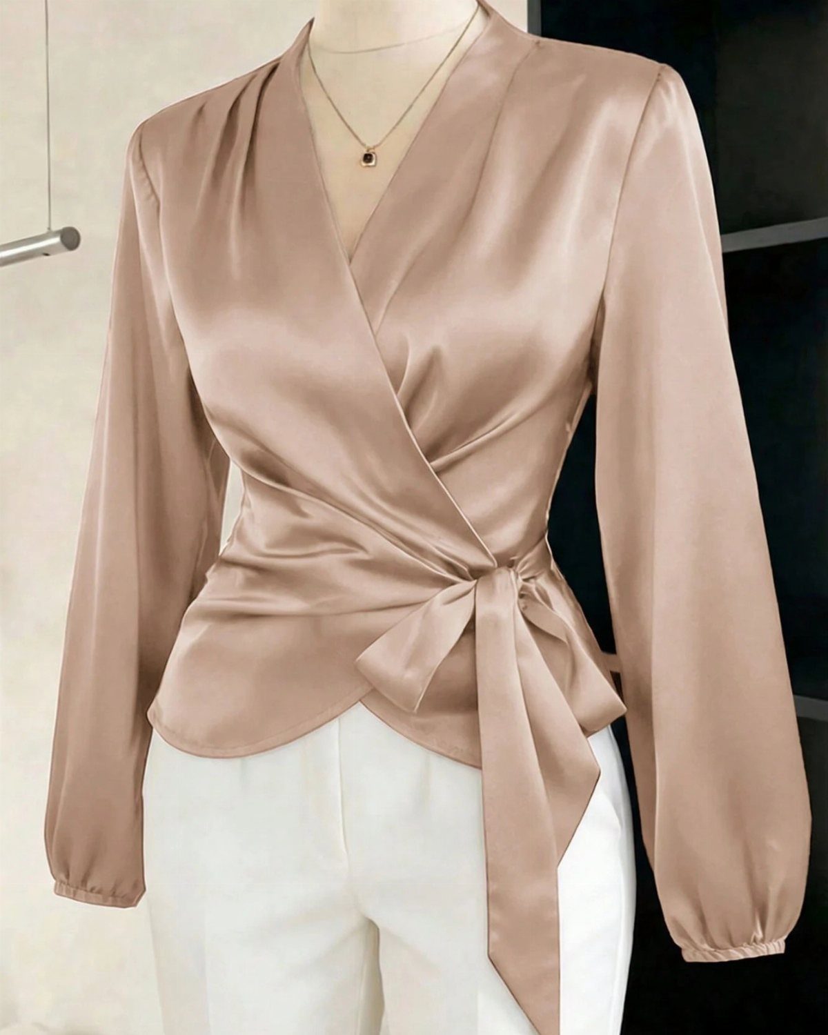 A person wearing a champagne satin wrap blouse with long sleeves and white trousers.