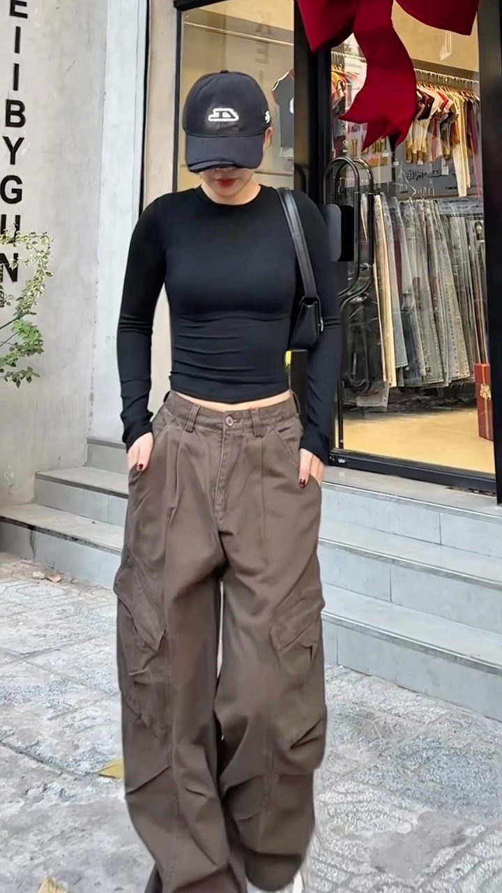 A person wearing a black long-sleeved top, baggy brown cargo pants, and a black cap.