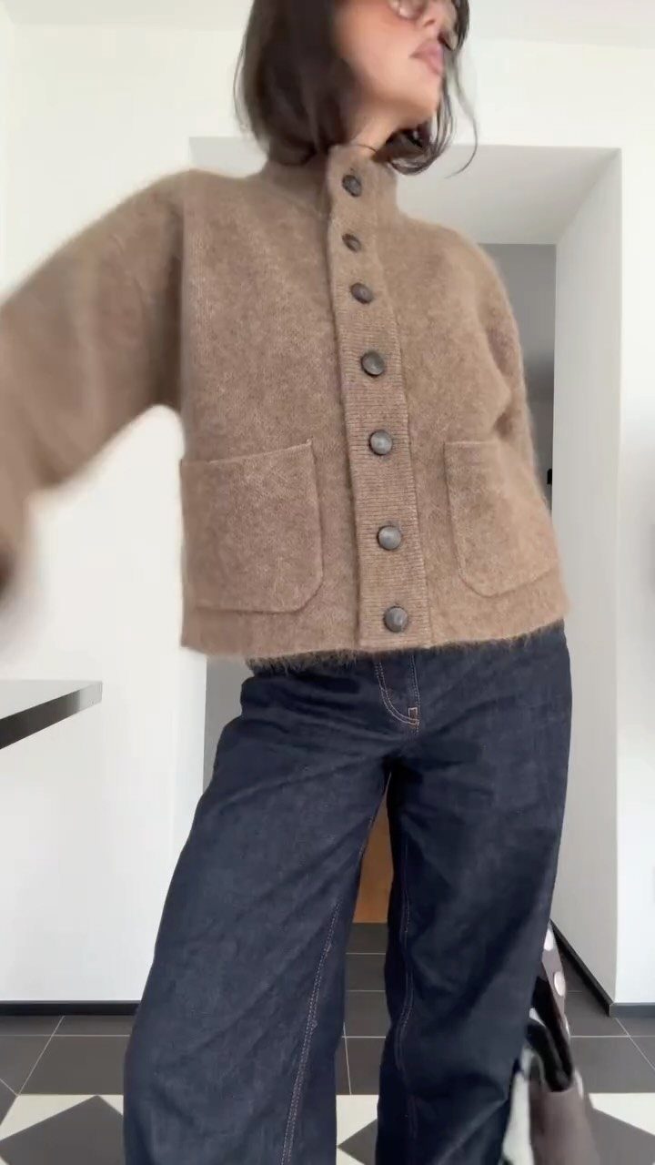 A person wearing a brown button-up wool cardigan and dark blue wide-leg denim jeans.