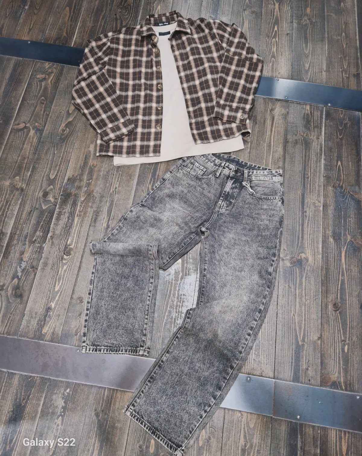 Plaid shirt and cream top laid above grey acid-wash jeans on a wooden floor.