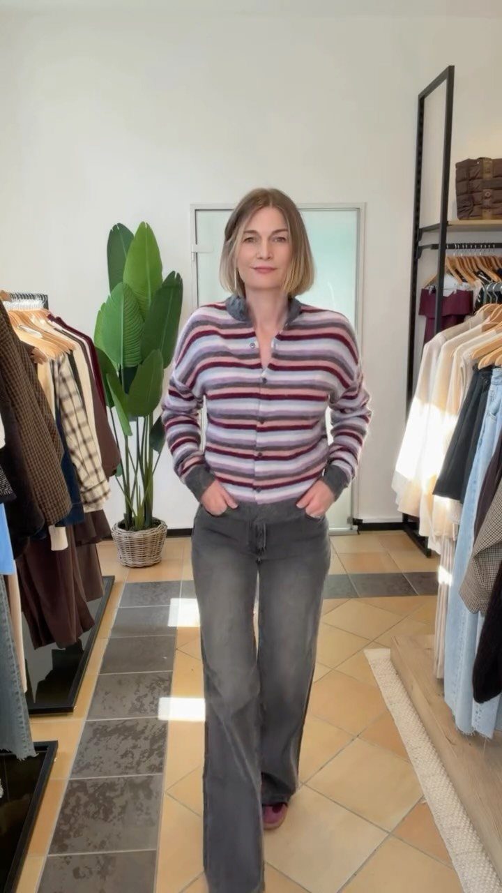 A woman wearing grey wide-leg jeans and a pink and navy striped long-sleeved top.