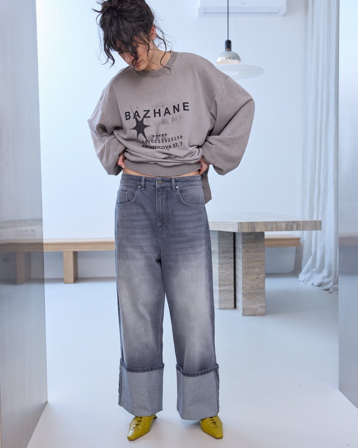 A person wearing a grey graphic sweatshirt and wide-leg grey cuffed jeans with yellow shoes.