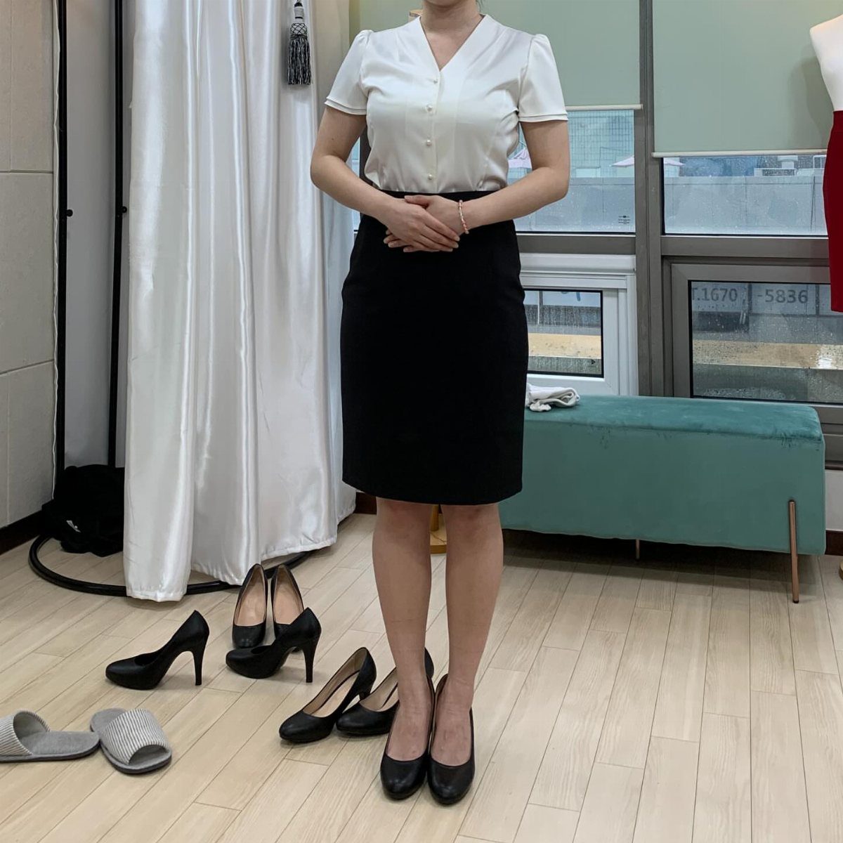 Woman wearing a white short-sleeved blouse and a black pencil skirt standing in a room.