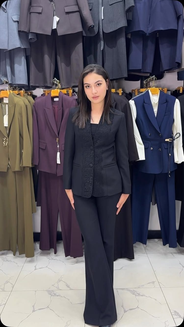 A woman posing in a black blazer and matching wide-leg trousers inside a clothing store.