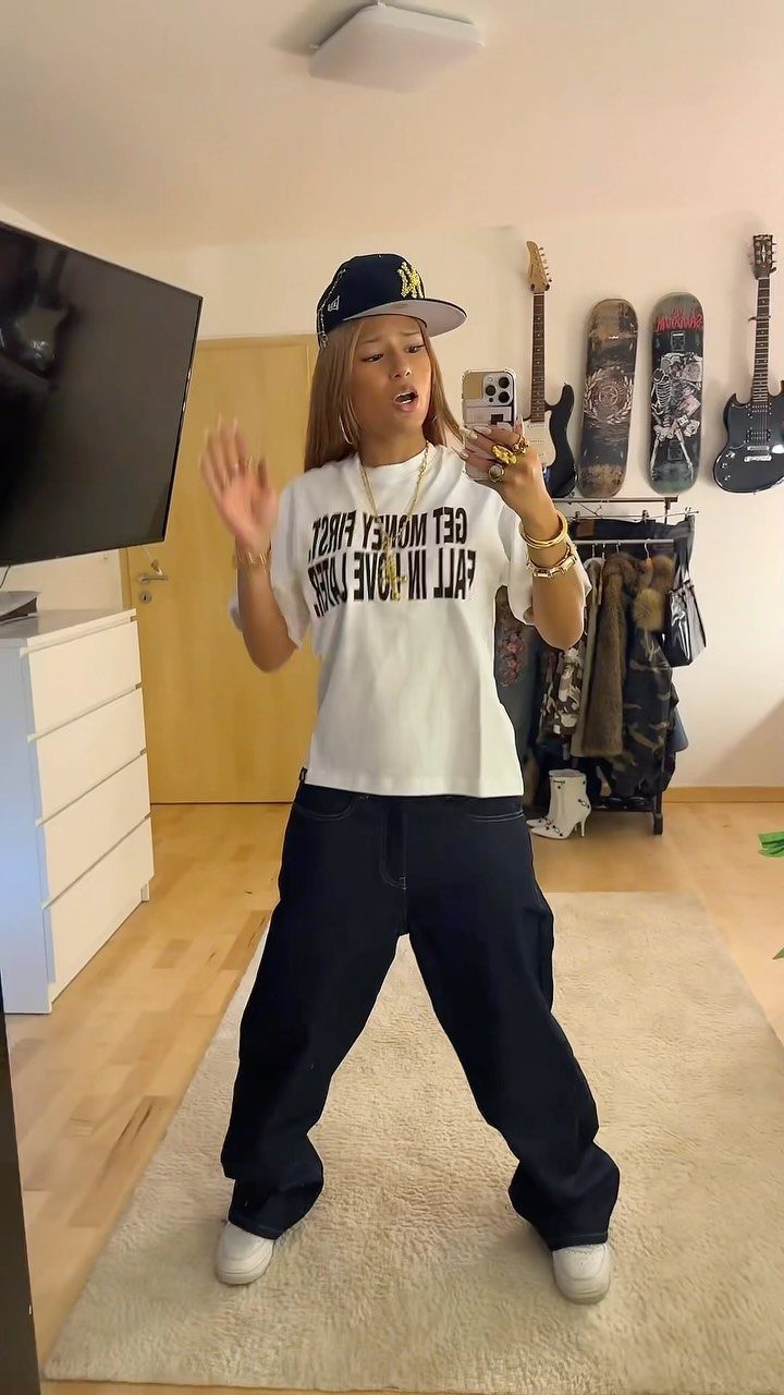 A woman posing in a white graphic t-shirt and dark wide-leg jeans.