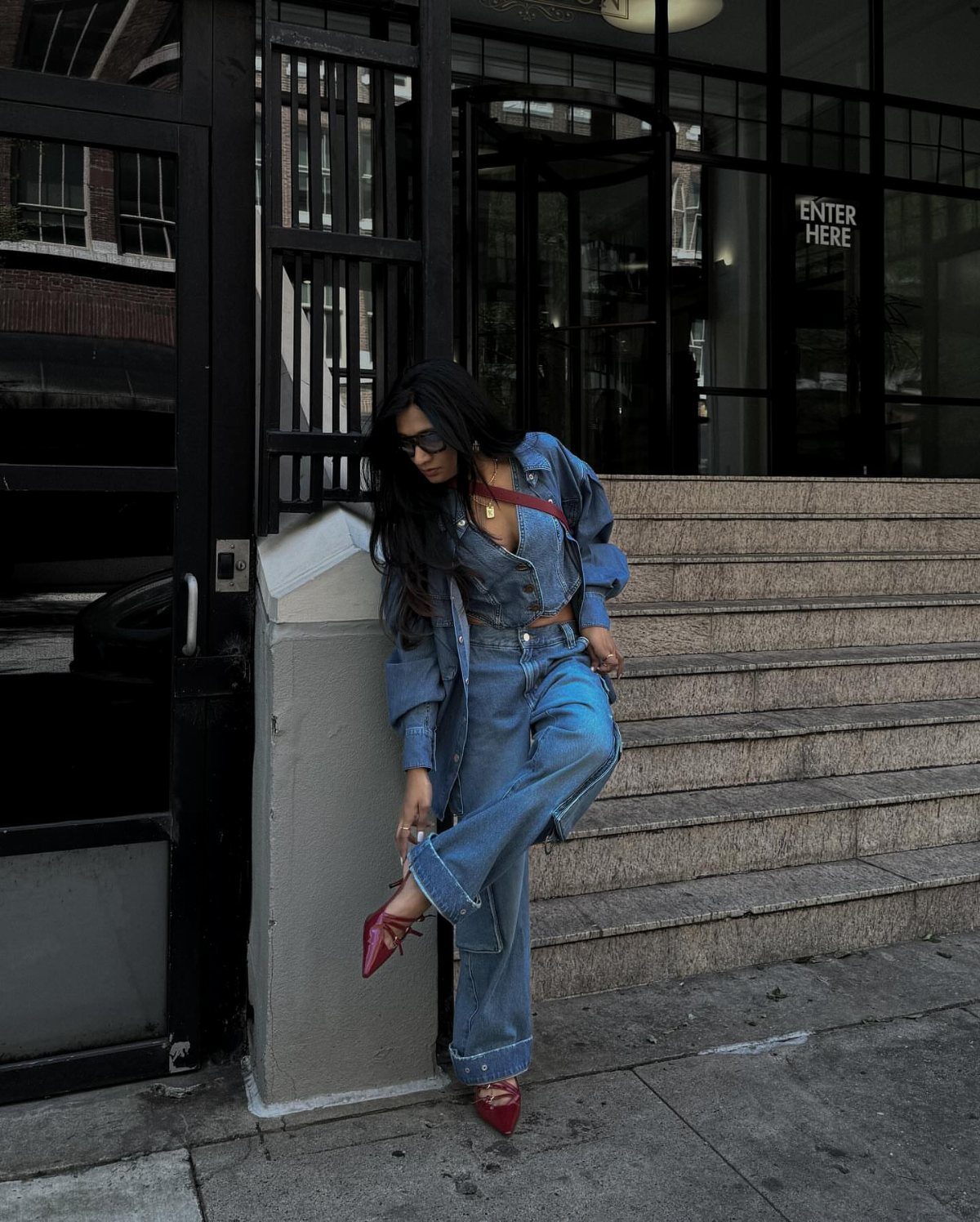 Woman in a denim jacket and wide-leg jeans posing by stone steps.