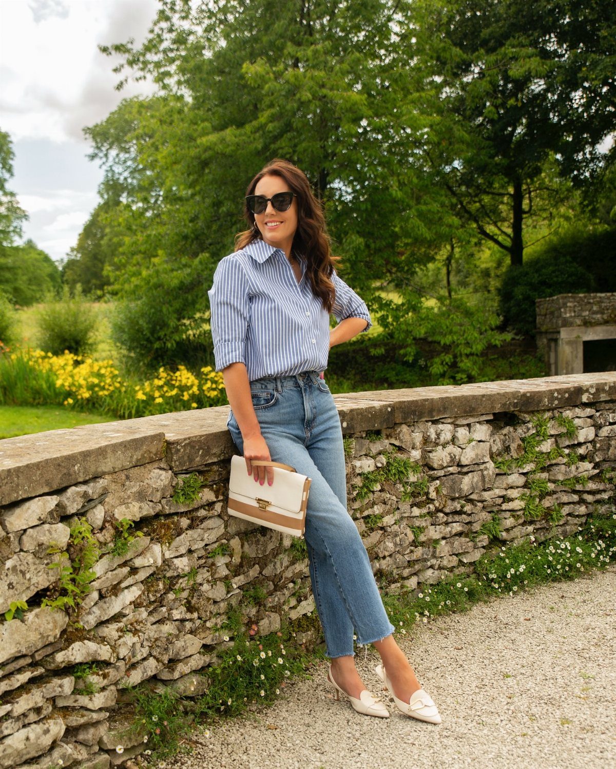 Woman in blue striped shirt and cropped jeans wearing white kitten heels outdoors.