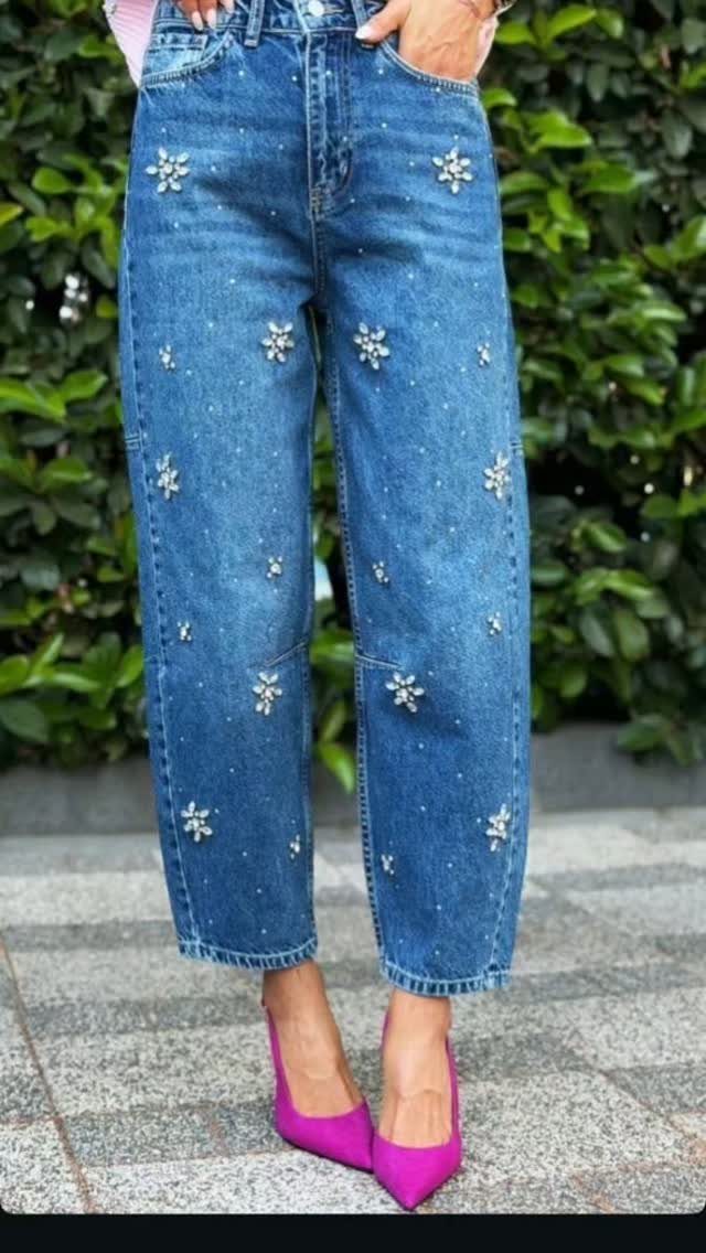 Person wearing embellished blue jeans and bright pink high heels standing on a stone path.