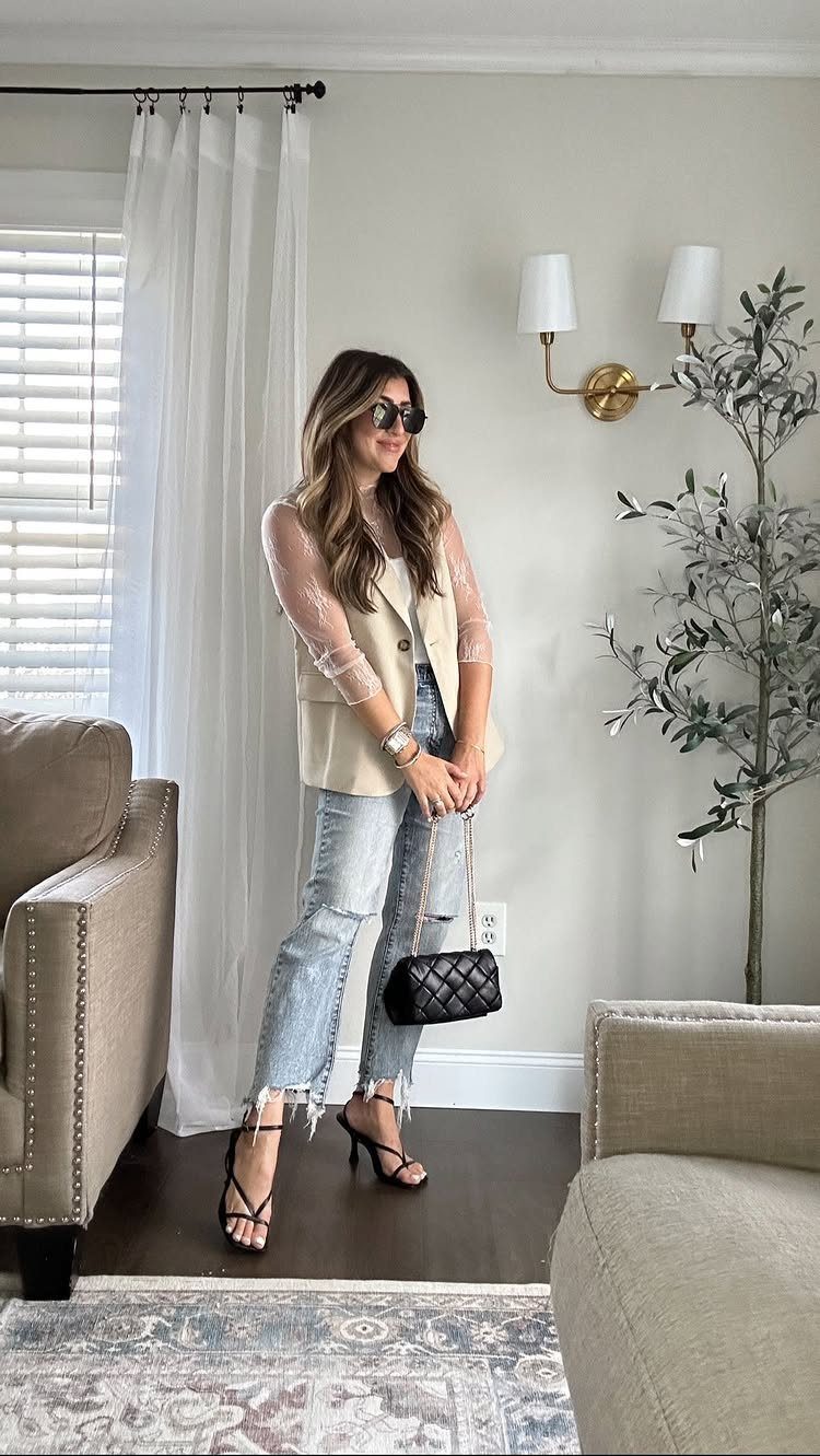 Woman wearing an embroidered top, cream vest, straight-leg jeans, and black strappy heels.