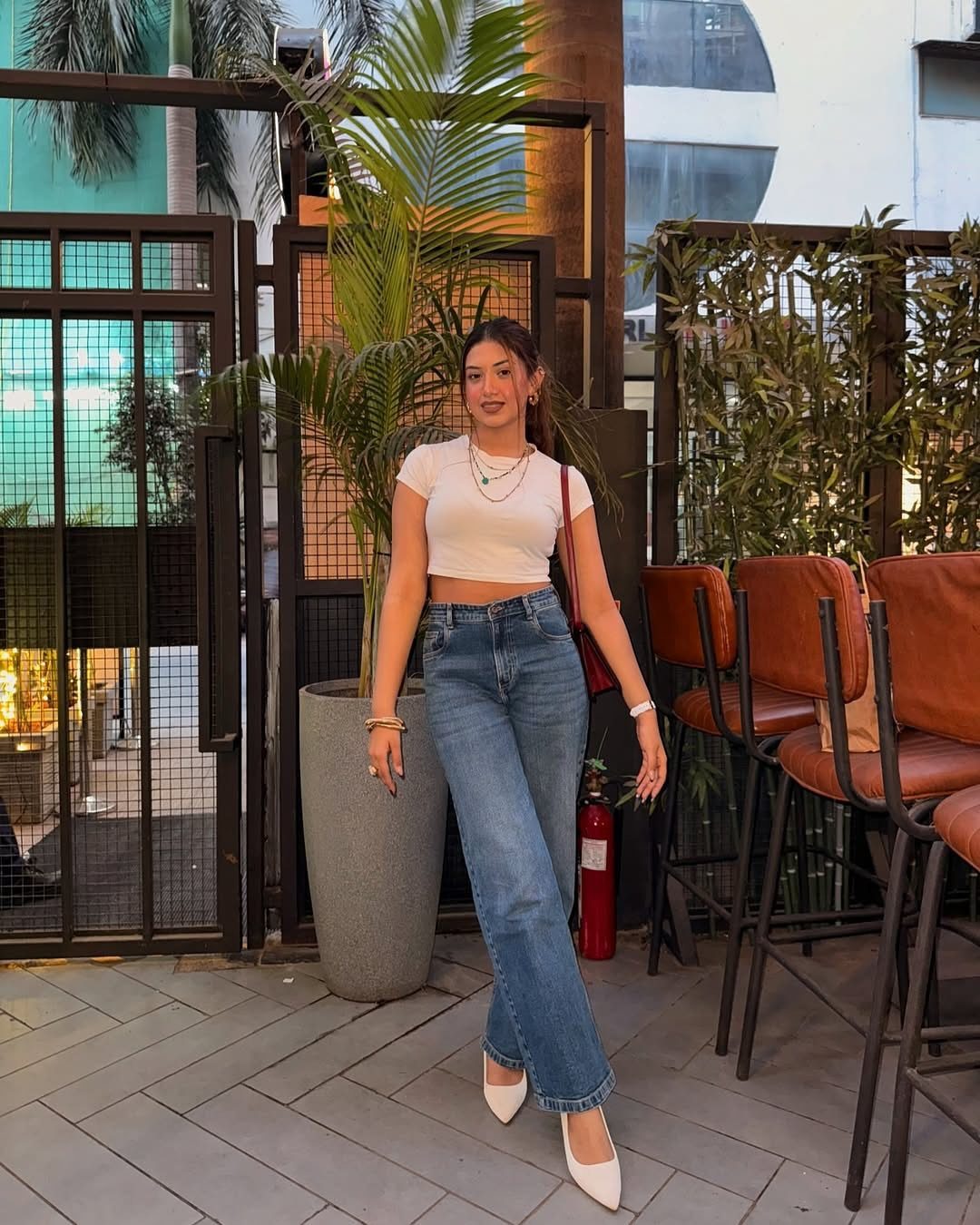 Woman wearing blue jeans and white pointed-toe high heels standing on a patio.