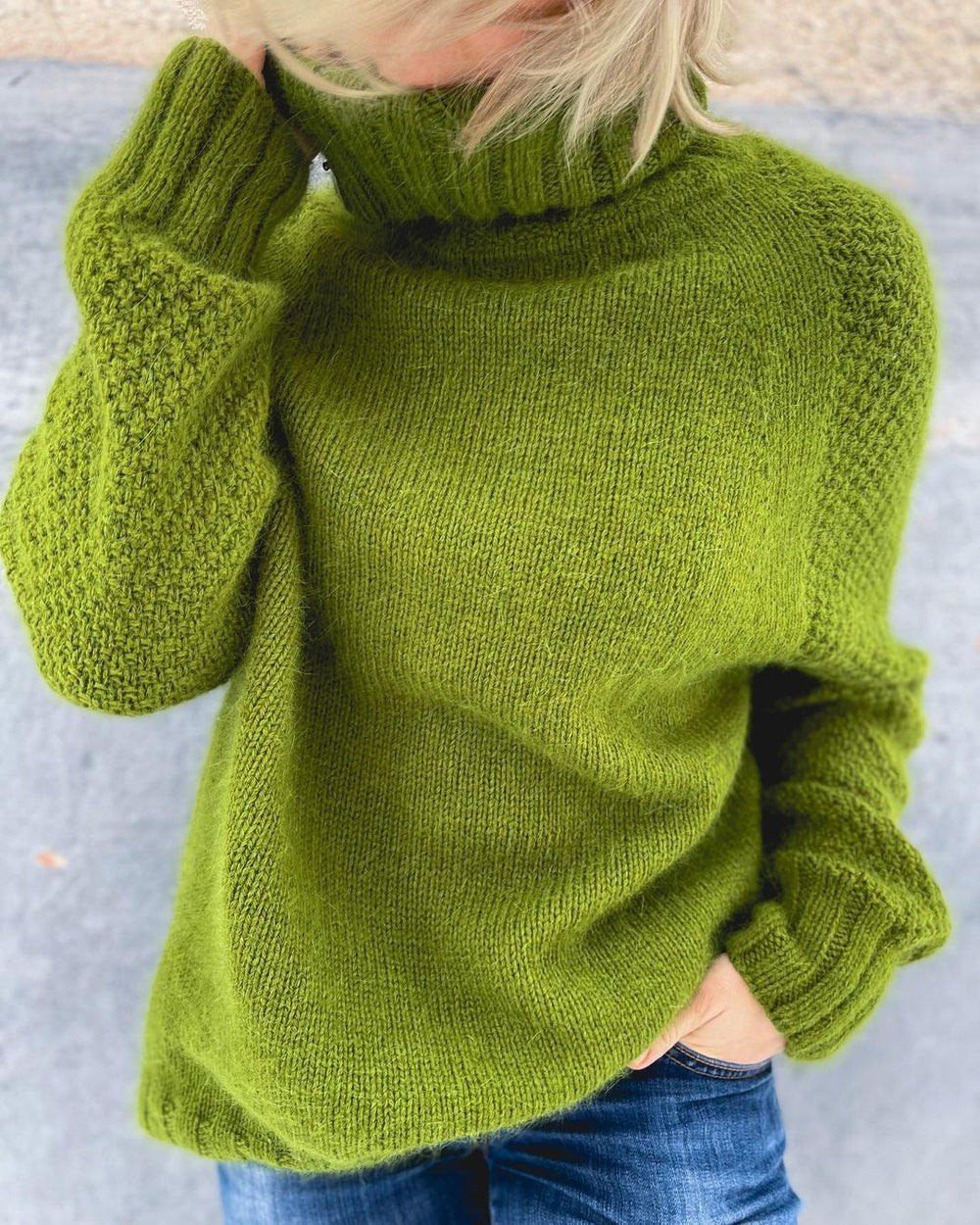 A person wearing a textured lime green knit turtleneck sweater and blue jeans.