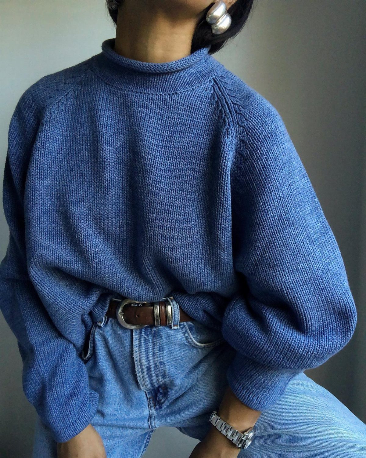 A person wearing a blue knit roll neck sweater and light blue denim jeans.