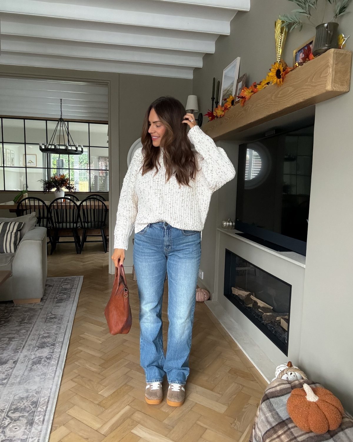 A woman wearing a textured white knit sweater and blue jeans standing in a living room.