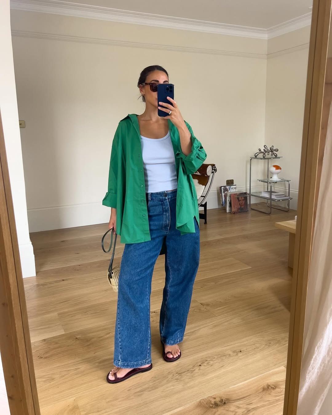 Woman in a green button-down shirt over a white tank top and wide-leg blue jeans.