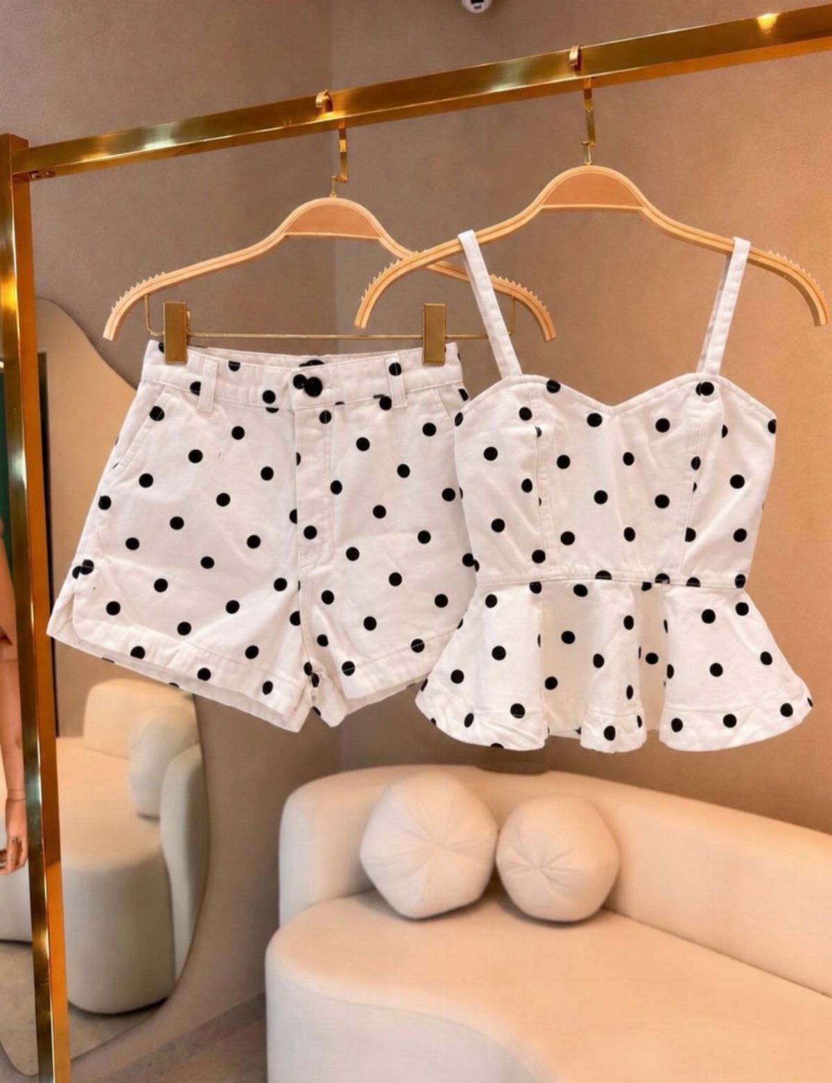 White polka dot denim shorts and a matching peplum top hanging on a gold rack.