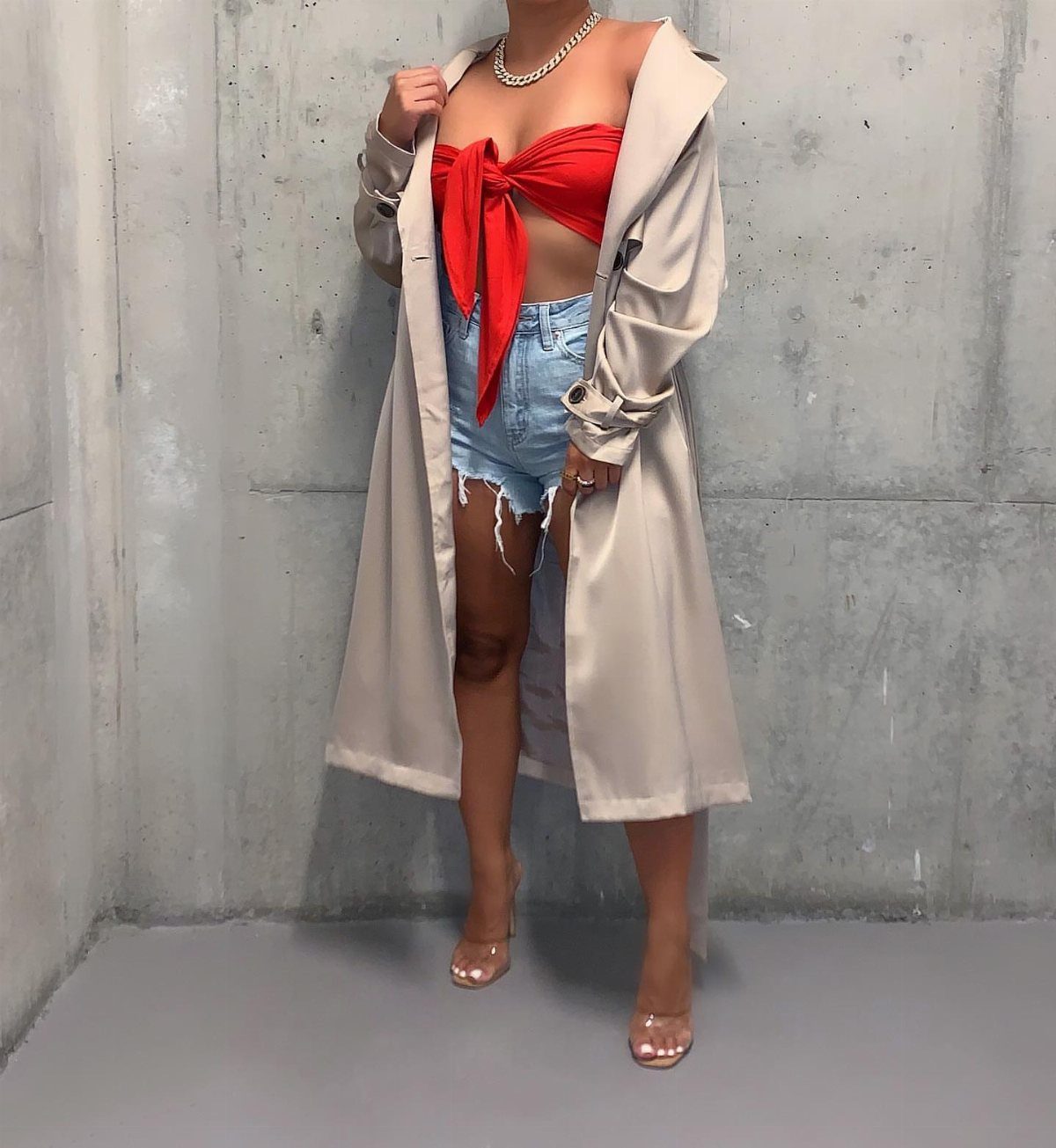 A person wearing denim shorts, a red crop top, and a long beige trench coat.