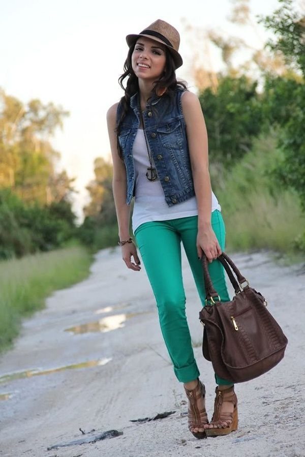 A woman posing in a denim vest, white t-shirt, and bright green pants outdoors.