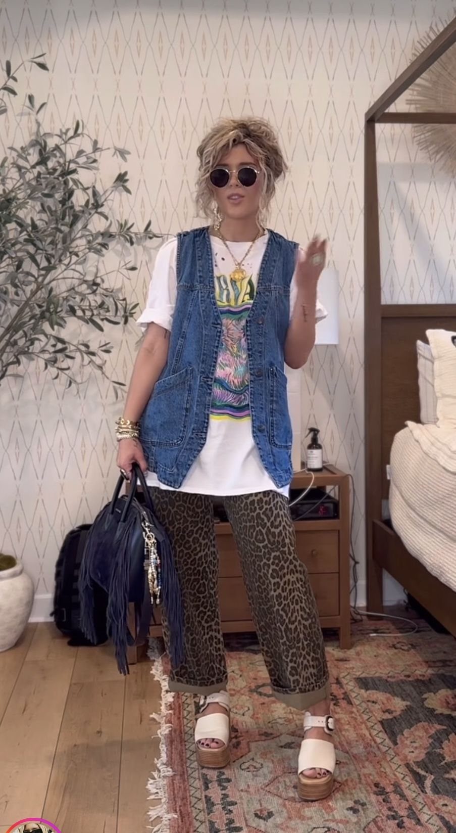 Woman posing in a denim vest, white graphic t-shirt, and leopard print trousers.