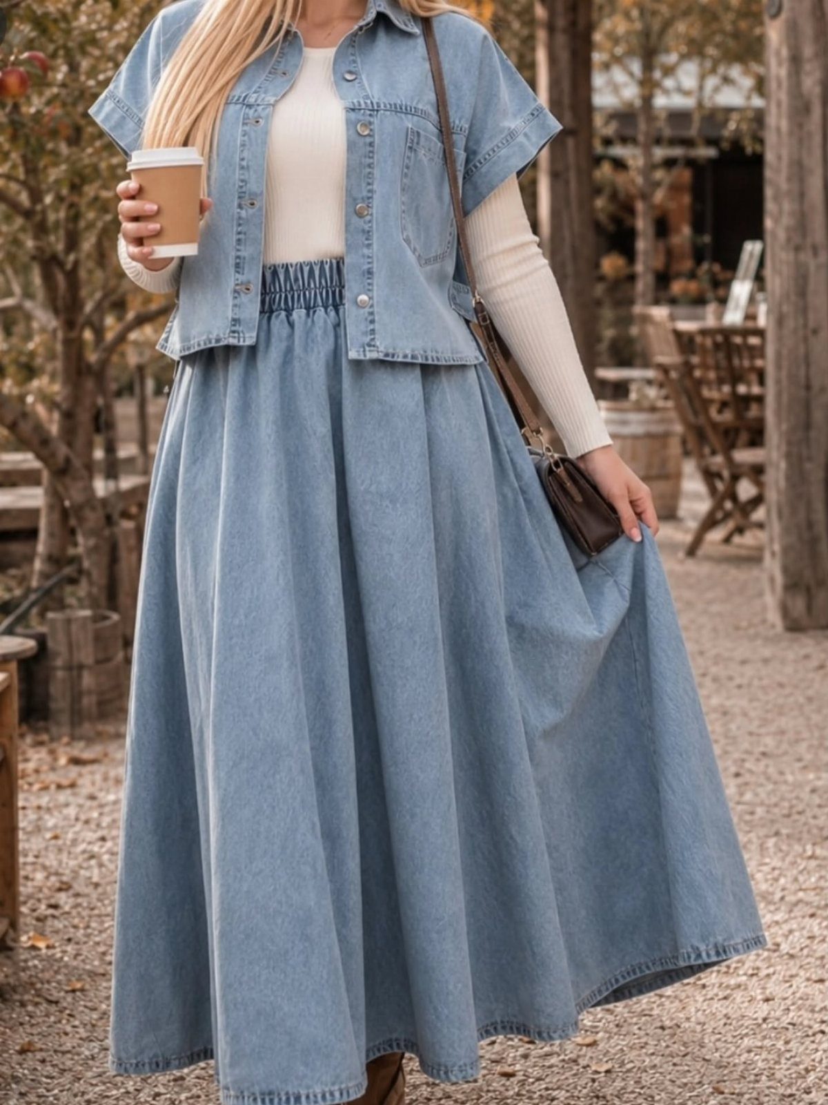 A person wearing a denim vest and a long denim maxi skirt while holding coffee.