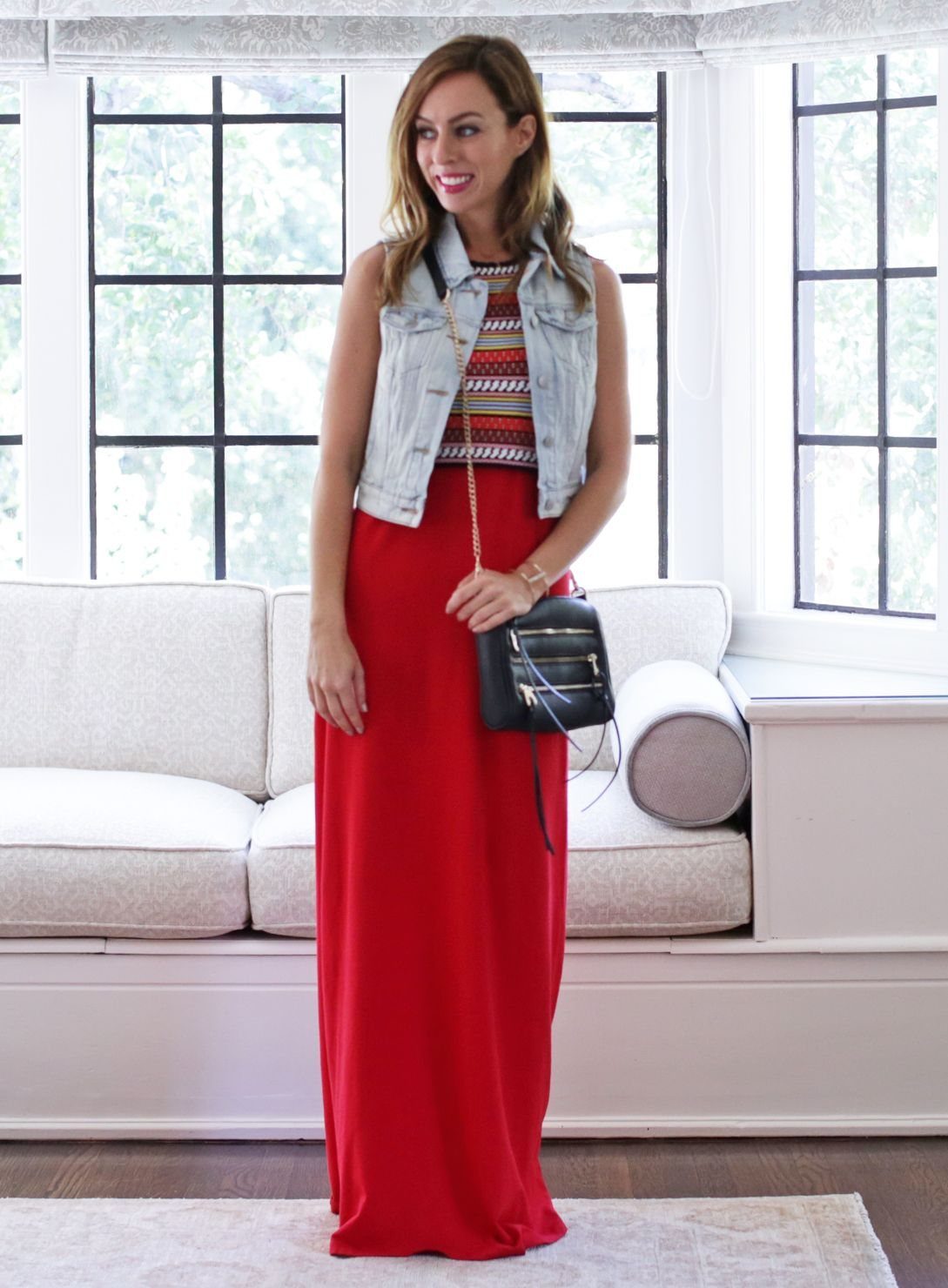 Woman wearing a light denim vest over a red maxi dress and patterned top.