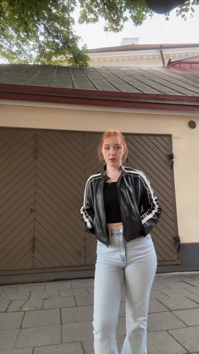 A woman wearing a black leather jacket and a black cropped top with light blue jeans.