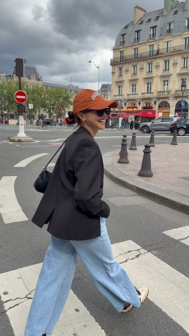 A woman in light blue jeans and a black blazer walking across a city street.