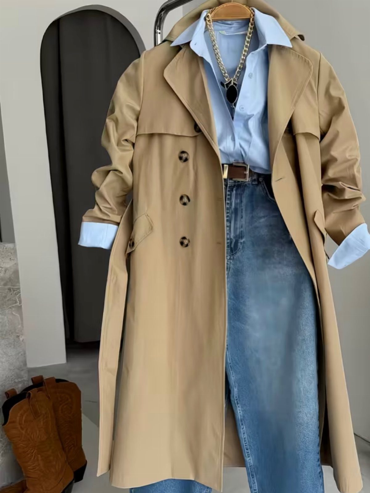 A tan trench coat worn over a light blue shirt and light blue denim jeans.