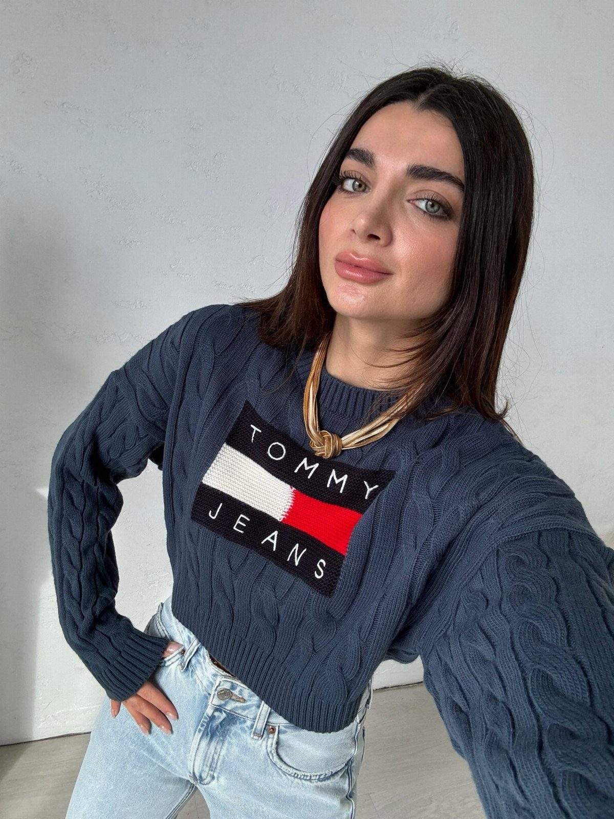 A woman wearing a navy blue Tommy Jeans sweater and light blue denim jeans.