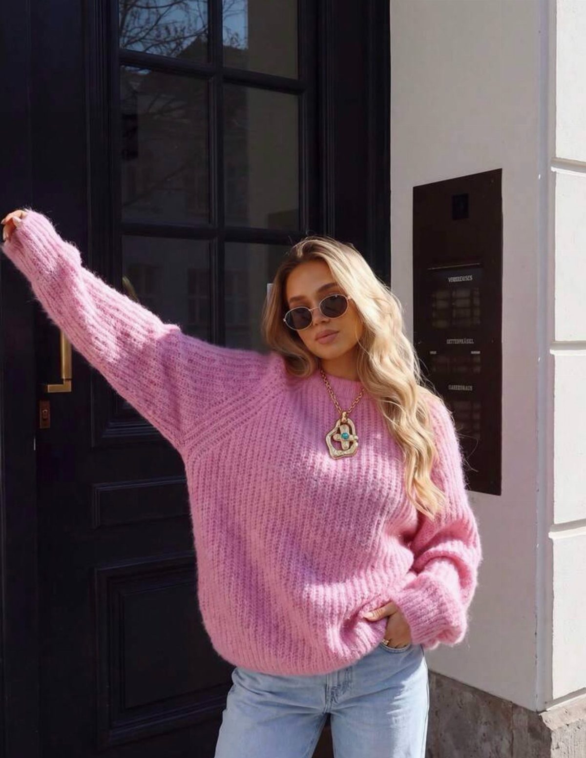 A woman in an oversized pink sweater and light blue jeans posing outdoors.