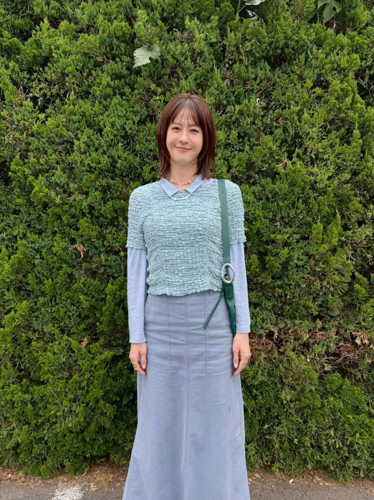 Woman wearing a textured light blue cropped top layered over a long-sleeved shirt and a matching skirt.