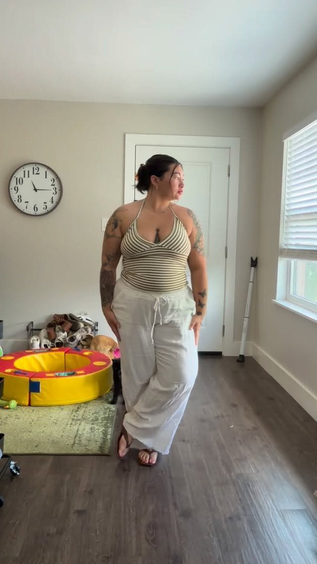 A woman wearing a striped halter top and white linen pants standing in a room.