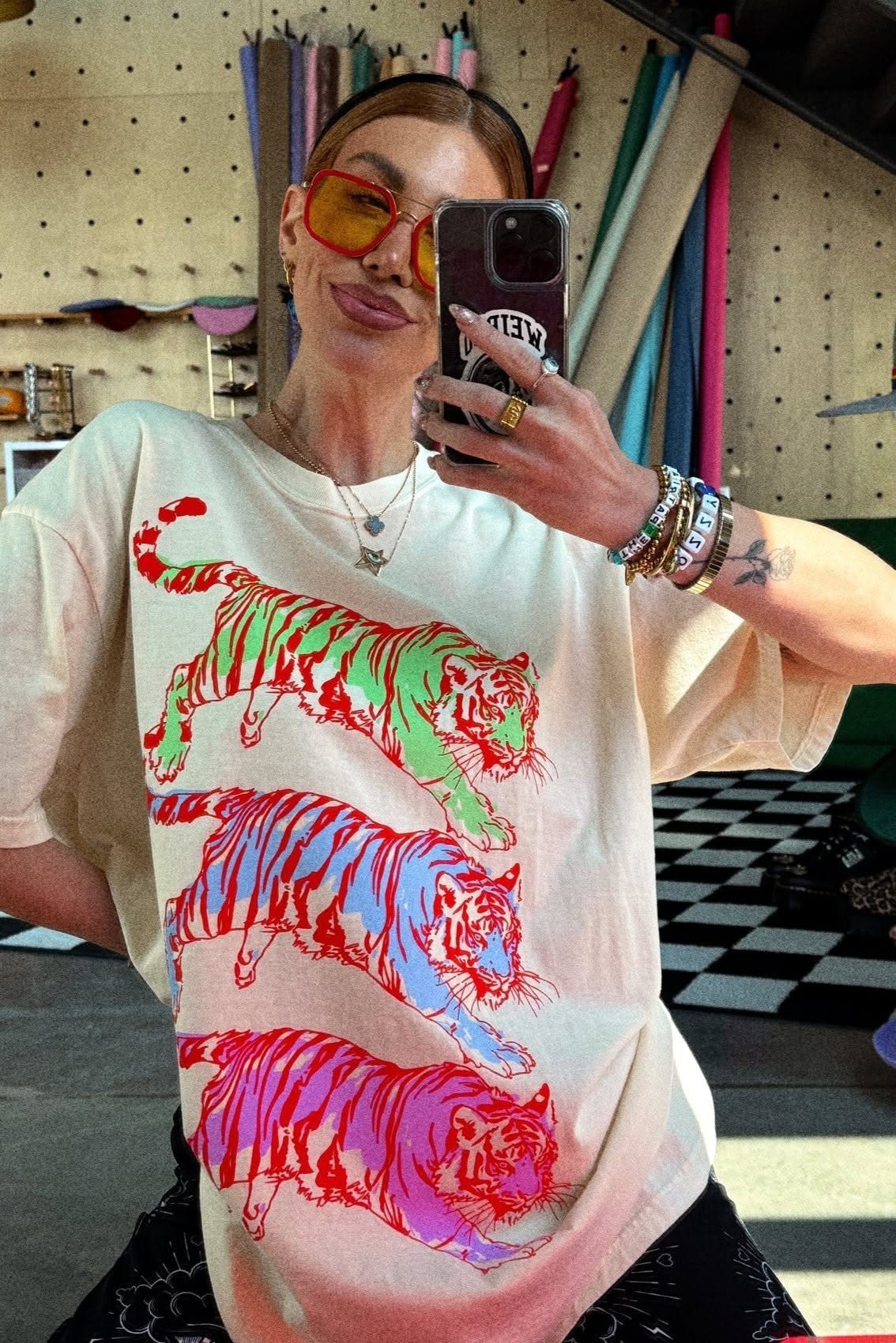 Woman in a cream oversized graphic t-shirt with colorful tiger prints taking a mirror selfie.